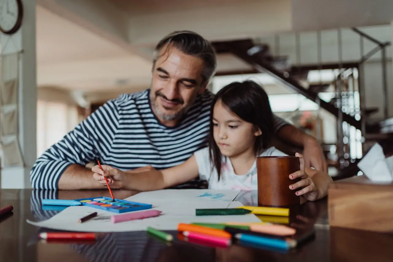 Father helps his daughter paint at home, representing family health insurance in Texas coverage for parents and kids.