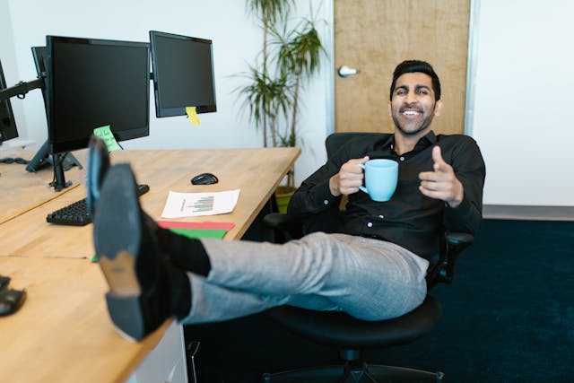 Happy entrepreneur relaxing with his feet on his desk, an ideal candidate for small business health insurance for one employee.