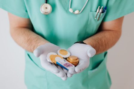 Doctor in scrubs holding coins and cash, illustrating HSA vs FSA healthcare savings options