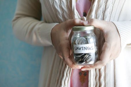 Woman holding a savings jar labeled "Savings" filled with coins, representing money saved through a High Deductible Health Plan