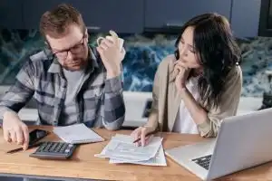 Couple reviewing health savings account rules and paperwork together at kitchen table with calculator and laptop